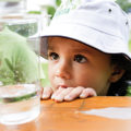 Junge mit Hut schaut sich ein Wasserglas an
