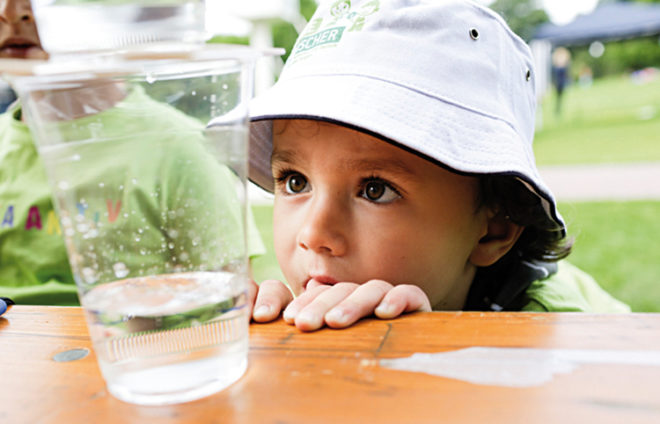 Junge mit Hut schaut sich ein Wasserglas an