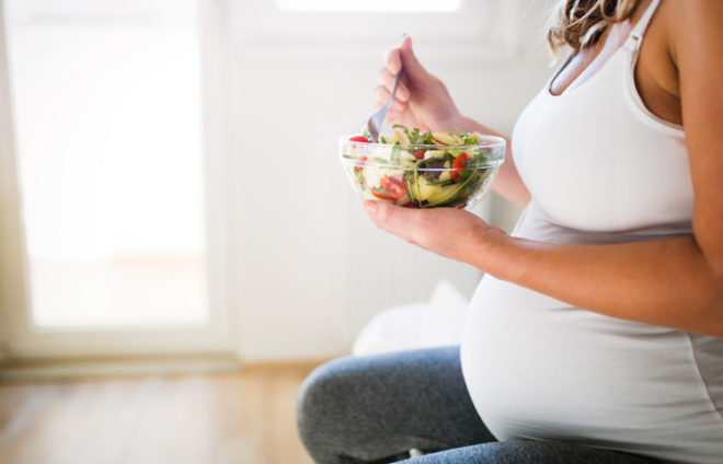 Schwangere Frau mit einer Salatschüssel in der Hand