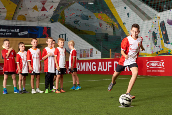 Fußballkind kickt gleich den Fußball, seine Gruppe schaut zu