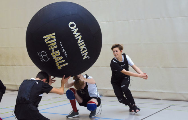 Zwei Jungs halten einen Kin-Ball hoch, ein anderer nimmt Anlauf zum Schlagen