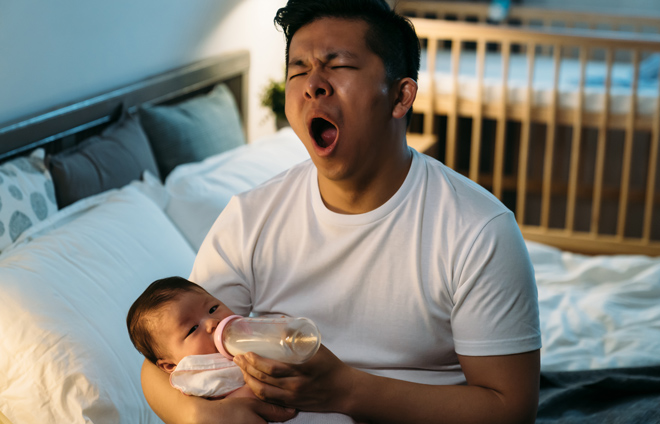Müder Vater füttert Baby mit Fläschen