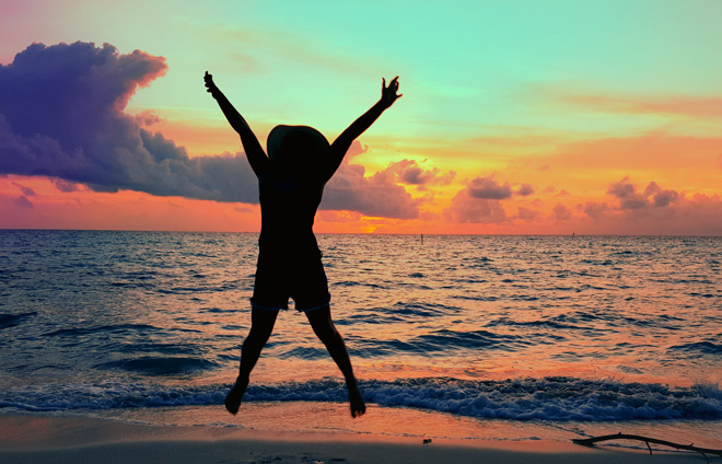 Kind springt vor Meer im Sonnenuntergang